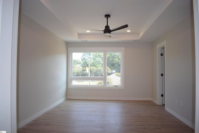 empty room with recessed lighting, a raised ceiling, light wood-style floors, ceiling fan, and baseboards