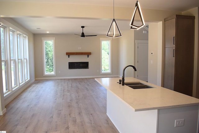 kitchen with a center island with sink, pendant lighting, light stone counters, and light hardwood / wood-style flooring