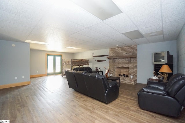 living room with light hardwood / wood-style flooring, a brick fireplace, and a drop ceiling