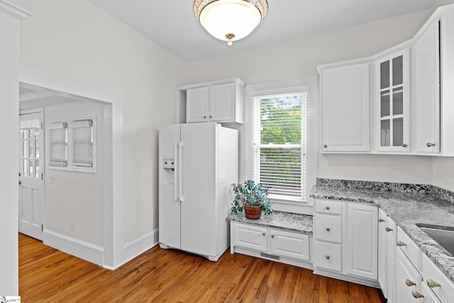 kitchen with white cabinets, white fridge with ice dispenser, light hardwood / wood-style floors, and light stone counters