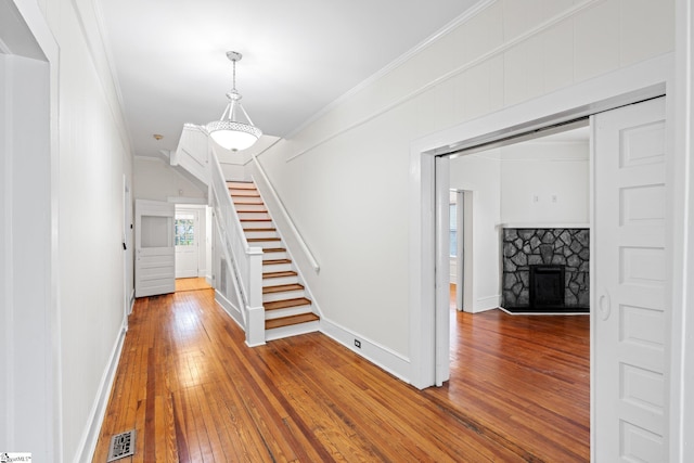 interior space featuring a stone fireplace, ornamental molding, and hardwood / wood-style floors