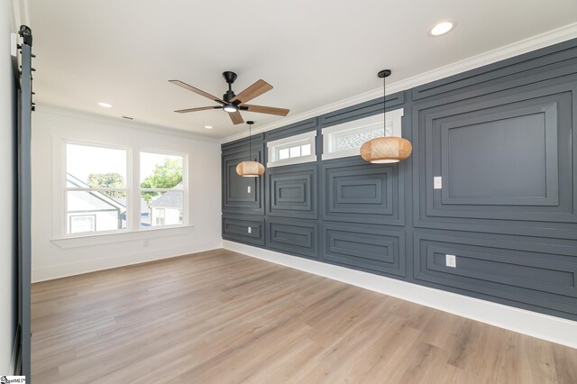 spare room with ornamental molding, wood-type flooring, ceiling fan, and a barn door