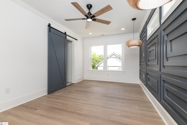 unfurnished bedroom featuring light hardwood / wood-style flooring, crown molding, and a barn door