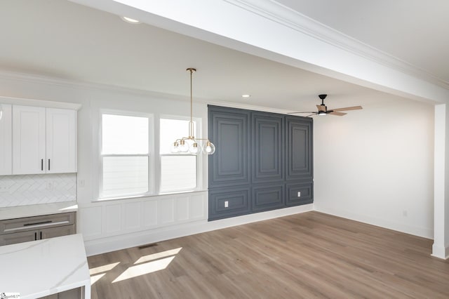 unfurnished living room featuring crown molding, ceiling fan with notable chandelier, and hardwood / wood-style flooring