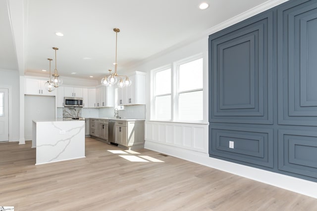 kitchen with light stone counters, white cabinetry, light hardwood / wood-style flooring, appliances with stainless steel finishes, and decorative light fixtures