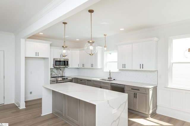 kitchen featuring appliances with stainless steel finishes, light stone counters, white cabinets, pendant lighting, and a center island