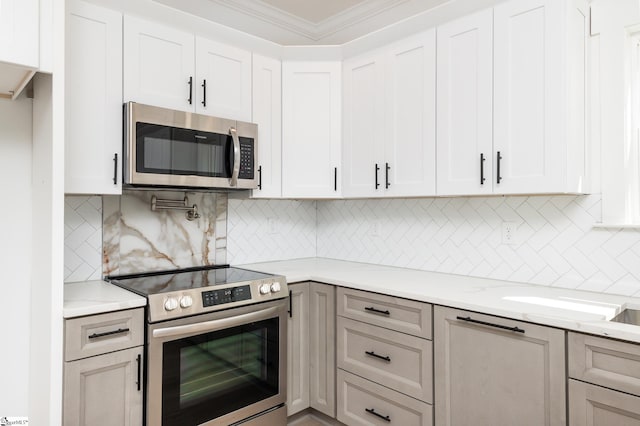 kitchen with light stone countertops, stainless steel appliances, ornamental molding, and white cabinetry