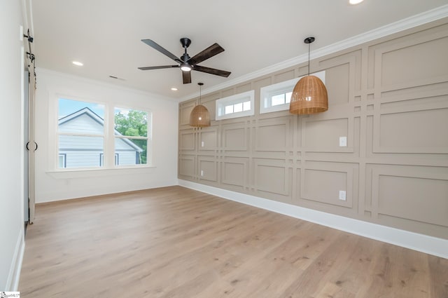 spare room featuring ornamental molding, ceiling fan, light hardwood / wood-style flooring, and a barn door