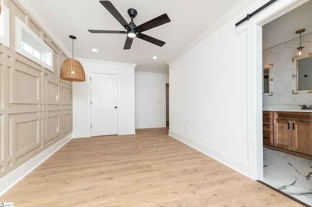 unfurnished living room featuring ceiling fan, sink, light hardwood / wood-style flooring, crown molding, and a barn door