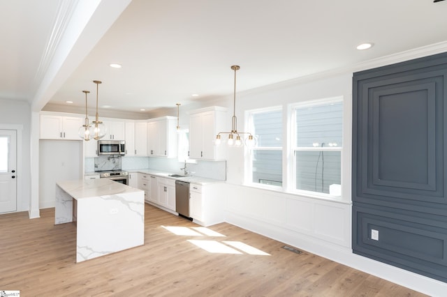 kitchen with white cabinets, a kitchen island, stainless steel appliances, decorative light fixtures, and sink