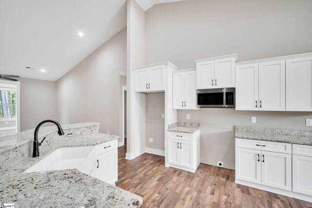 kitchen with light stone counters, high vaulted ceiling, white cabinets, wood-type flooring, and sink