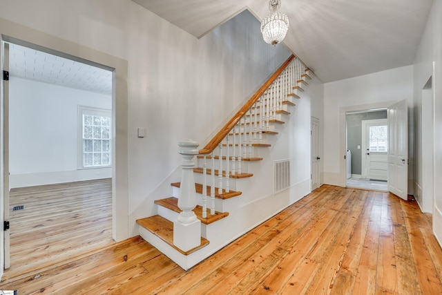 stairs featuring wood-type flooring and an inviting chandelier