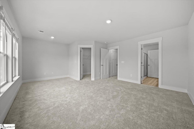 unfurnished bedroom with a spacious closet, connected bathroom, a closet, and light carpet