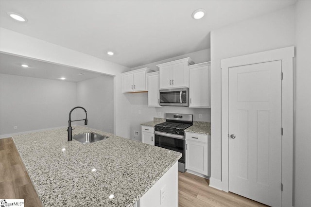 kitchen with white cabinets, an island with sink, sink, stainless steel appliances, and light hardwood / wood-style floors