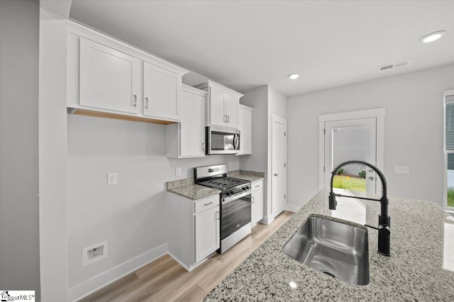 kitchen featuring white cabinets, light stone countertops, sink, appliances with stainless steel finishes, and light wood-type flooring