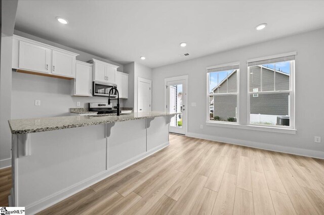 kitchen with a breakfast bar, light hardwood / wood-style floors, white cabinets, appliances with stainless steel finishes, and light stone countertops