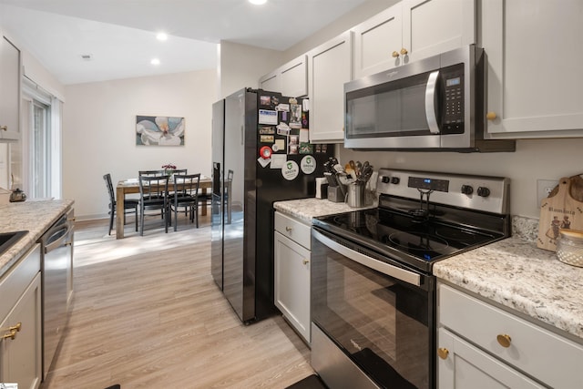 kitchen with light stone countertops, appliances with stainless steel finishes, light wood-type flooring, and white cabinetry