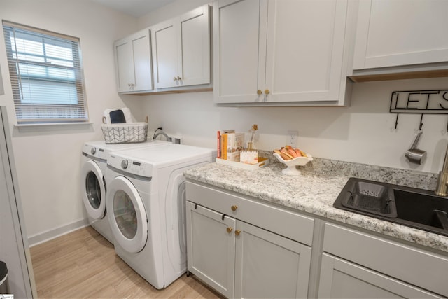 laundry room with cabinets, light wood-type flooring, sink, and washing machine and dryer