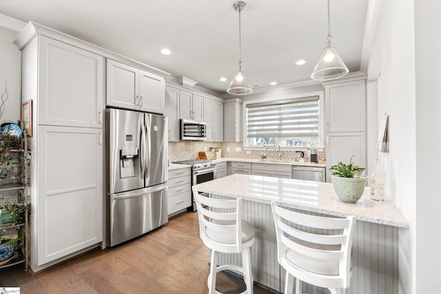 kitchen with light wood-type flooring, light stone countertops, a breakfast bar, hanging light fixtures, and appliances with stainless steel finishes