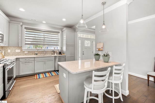 kitchen featuring light hardwood / wood-style floors, light stone counters, sink, appliances with stainless steel finishes, and a kitchen bar