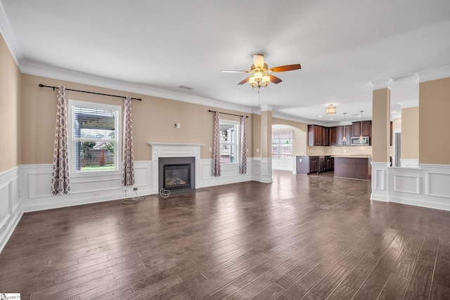 unfurnished living room with ceiling fan, a healthy amount of sunlight, crown molding, and dark hardwood / wood-style floors