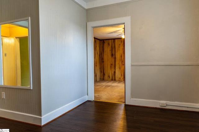 empty room with ornamental molding, wooden walls, ceiling fan, and dark wood-type flooring