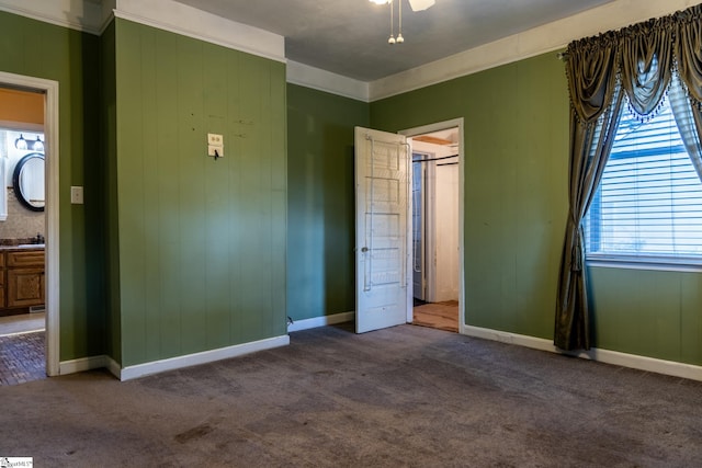 unfurnished bedroom with ornamental molding, ensuite bathroom, wood walls, and carpet