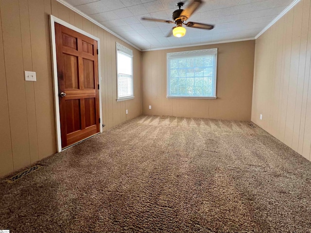 unfurnished room featuring ornamental molding, wooden walls, ceiling fan, and carpet