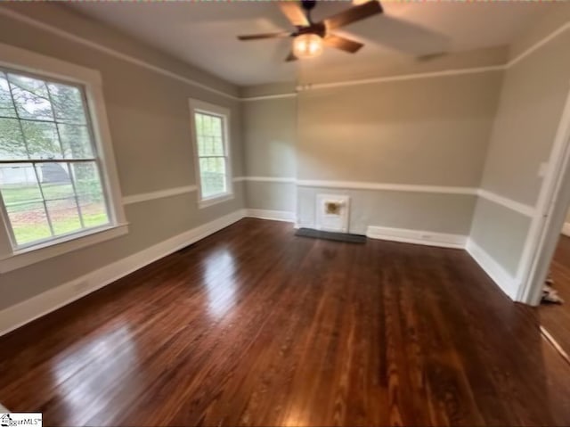 empty room with a healthy amount of sunlight, ceiling fan, and dark hardwood / wood-style flooring