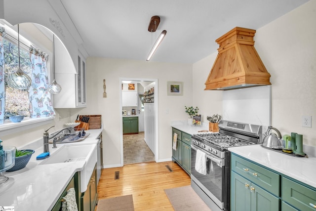 kitchen with light stone countertops, custom range hood, stainless steel gas stove, light hardwood / wood-style floors, and green cabinets