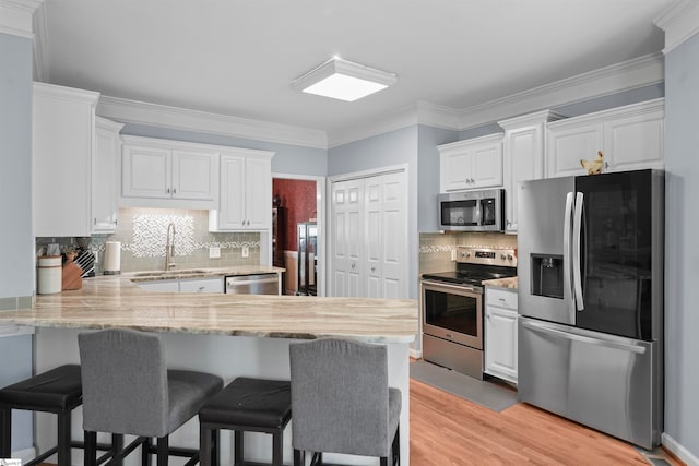 kitchen with white cabinets, sink, kitchen peninsula, stainless steel appliances, and light hardwood / wood-style floors