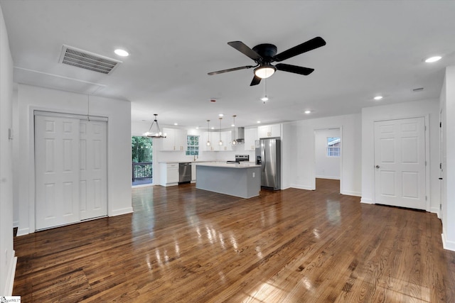 unfurnished living room featuring ceiling fan with notable chandelier and dark wood-type flooring