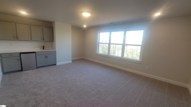 kitchen featuring baseboards, light colored carpet, light countertops, gray cabinetry, and backsplash