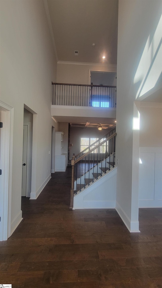 corridor featuring dark wood finished floors, stairway, a high ceiling, ornamental molding, and baseboards