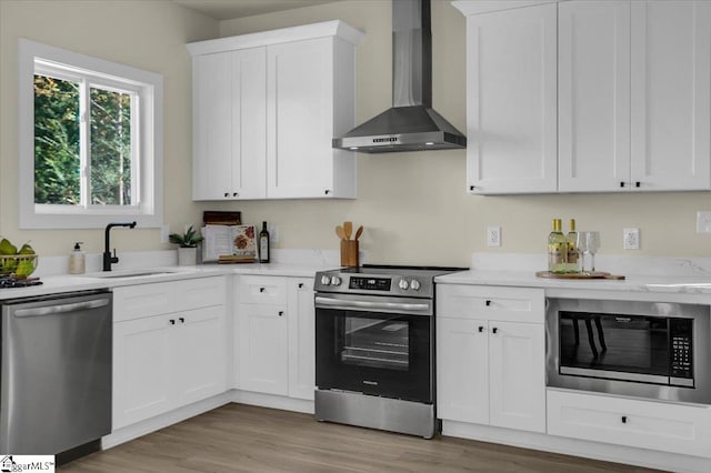 kitchen featuring light wood-type flooring, wall chimney range hood, white cabinetry, and stainless steel appliances