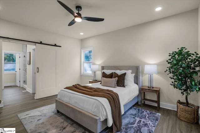 bedroom featuring ceiling fan, a barn door, multiple windows, and dark hardwood / wood-style flooring