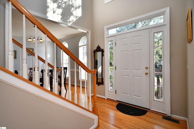 entryway featuring wood-type flooring, ornamental molding, an inviting chandelier, and a wealth of natural light