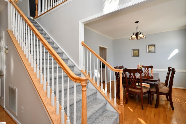 staircase featuring ornamental molding, hardwood / wood-style floors, and an inviting chandelier