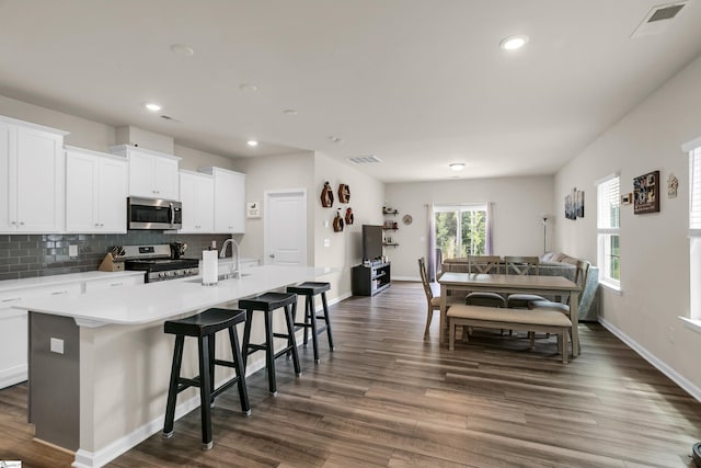 kitchen with a center island with sink, white cabinetry, stainless steel appliances, and dark hardwood / wood-style flooring