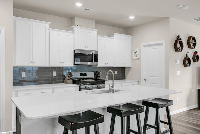 kitchen with white cabinets, a center island with sink, appliances with stainless steel finishes, and light hardwood / wood-style floors