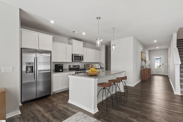 kitchen featuring stainless steel appliances, stone counters, white cabinets, and an island with sink