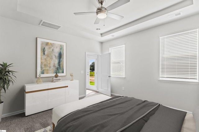 carpeted bedroom with ceiling fan and a raised ceiling