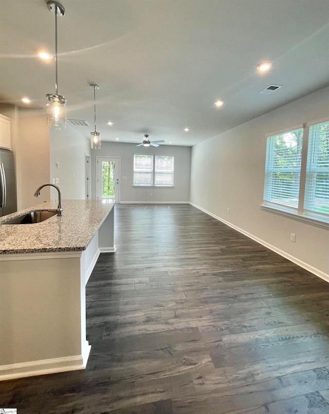 kitchen featuring light stone counters, hanging light fixtures, sink, dark wood-type flooring, and ceiling fan