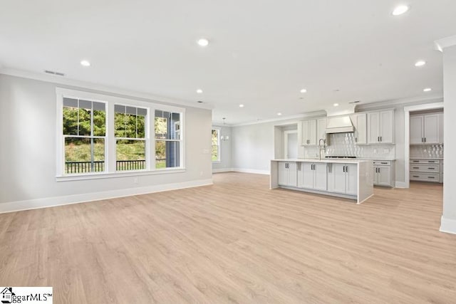 unfurnished living room featuring light hardwood / wood-style floors, ornamental molding, and sink