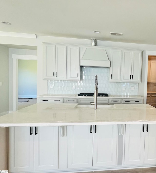 kitchen featuring a spacious island, white cabinetry, custom range hood, and tasteful backsplash