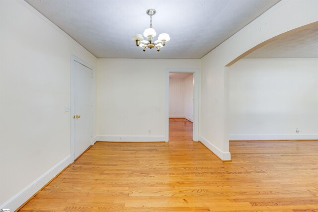 spare room featuring light wood-type flooring and a notable chandelier