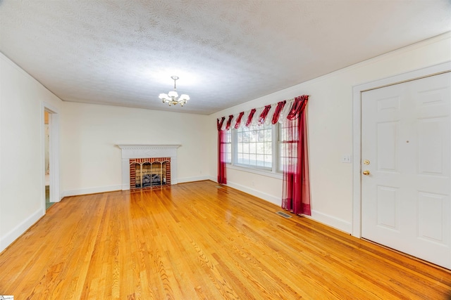 unfurnished living room with wood-type flooring, a notable chandelier, a brick fireplace, and a textured ceiling