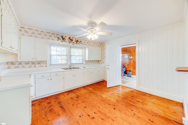 kitchen featuring ceiling fan, white cabinets, wood walls, sink, and light hardwood / wood-style flooring