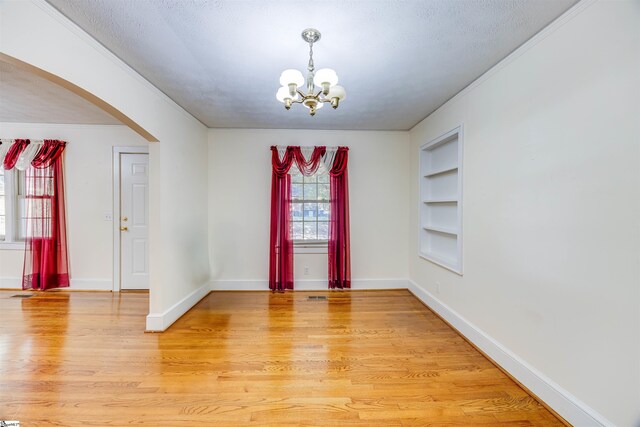 empty room with ornamental molding, a notable chandelier, wood-type flooring, and a textured ceiling