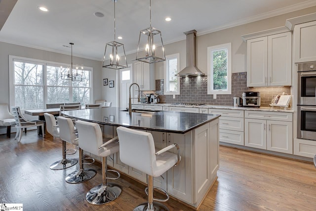 kitchen featuring a center island with sink, wall chimney exhaust hood, light hardwood / wood-style floors, and white cabinets